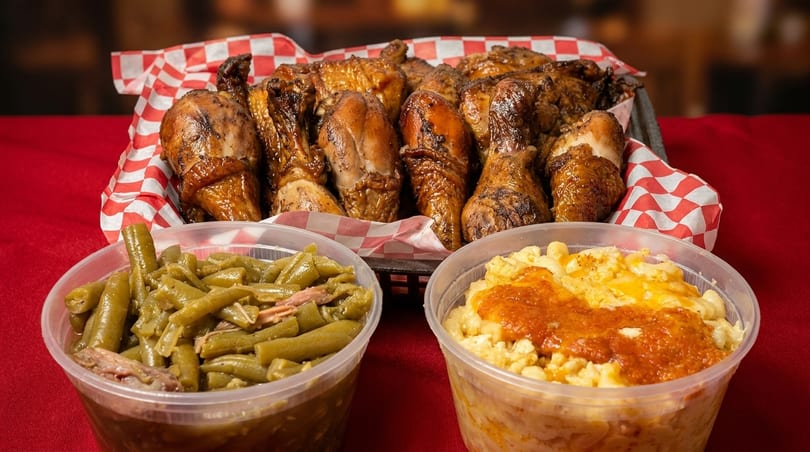 A basket of roasted chicken pieces, with sides of green beans and mac and cheese.
