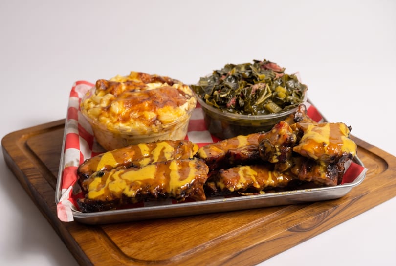 Ribs with mustard sauce, mac and cheese, and collard greens on a metal tray.