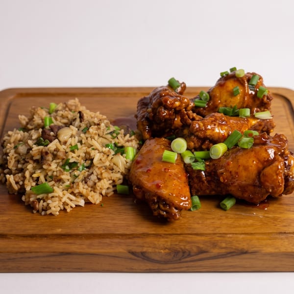 Glazed chicken wings and savory rice with green onions on a wooden serving board.