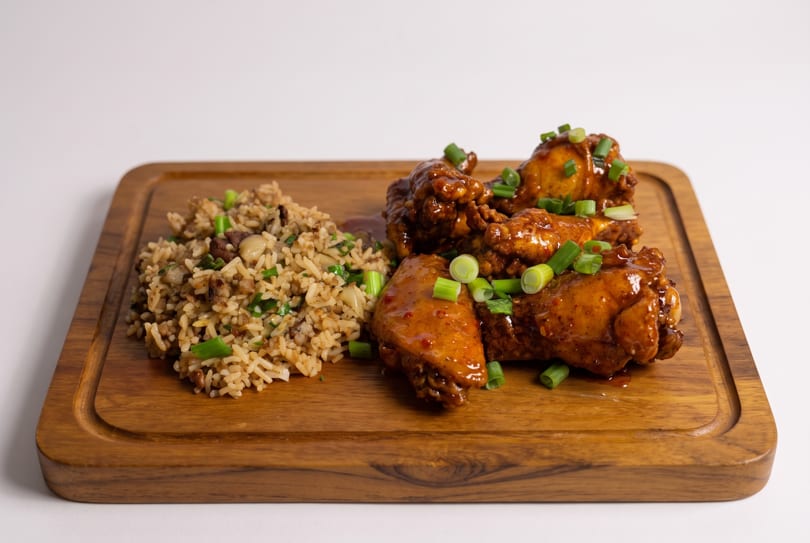 Glazed chicken wings and savory rice with green onions on a wooden serving board.