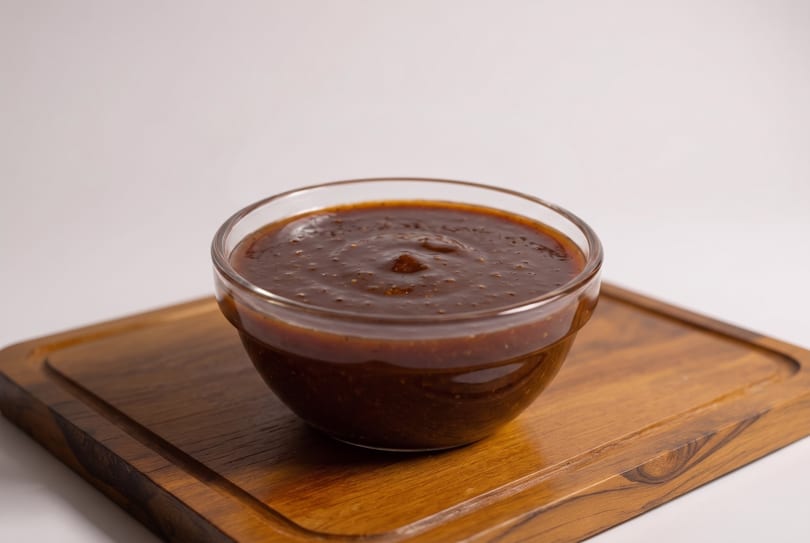 Thick, dark brown sauce in a clear glass bowl on a wooden board.