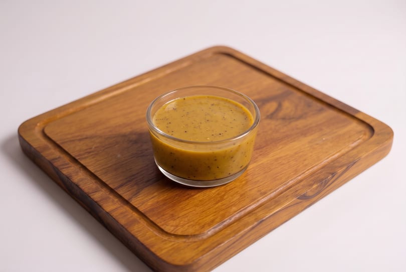 Small glass of speckled brown sauce on a wooden serving board.