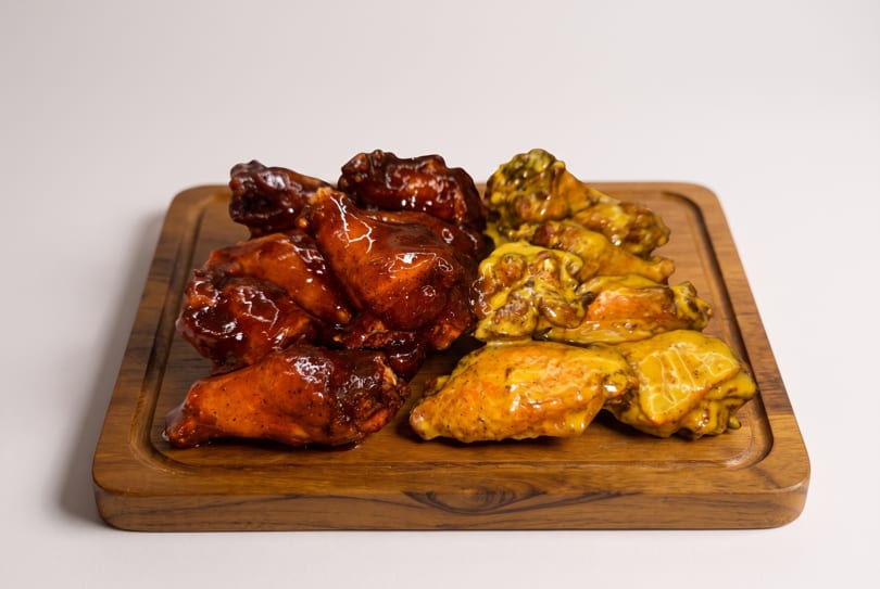 Glazed BBQ and yellow-sauced chicken wings arranged on a wooden serving board.