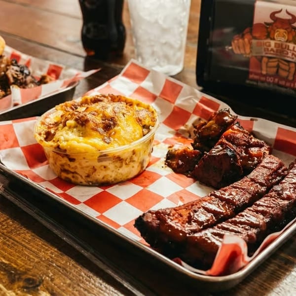 Big Bull Bar-B-Q'N ribs, mac and cheese, and a pulled pork sandwich on a wooden table.