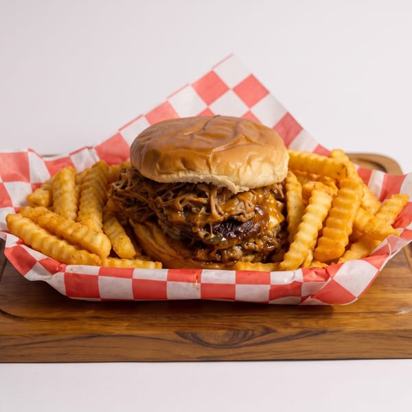 Pulled pork sandwich with cheese and crinkle-cut fries in a red and white checkered basket.