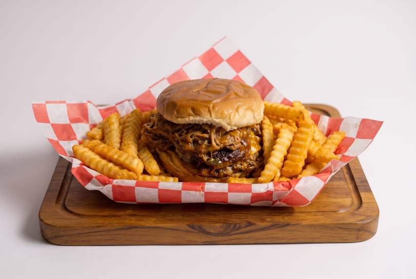 Pulled pork sandwich with cheese and crinkle-cut fries in a red and white checkered basket.